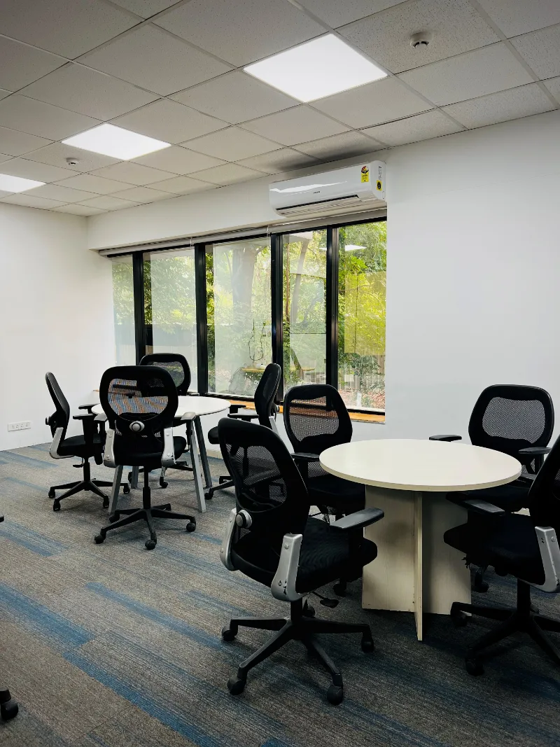 An open meeting area with round tables and windows onto trees.