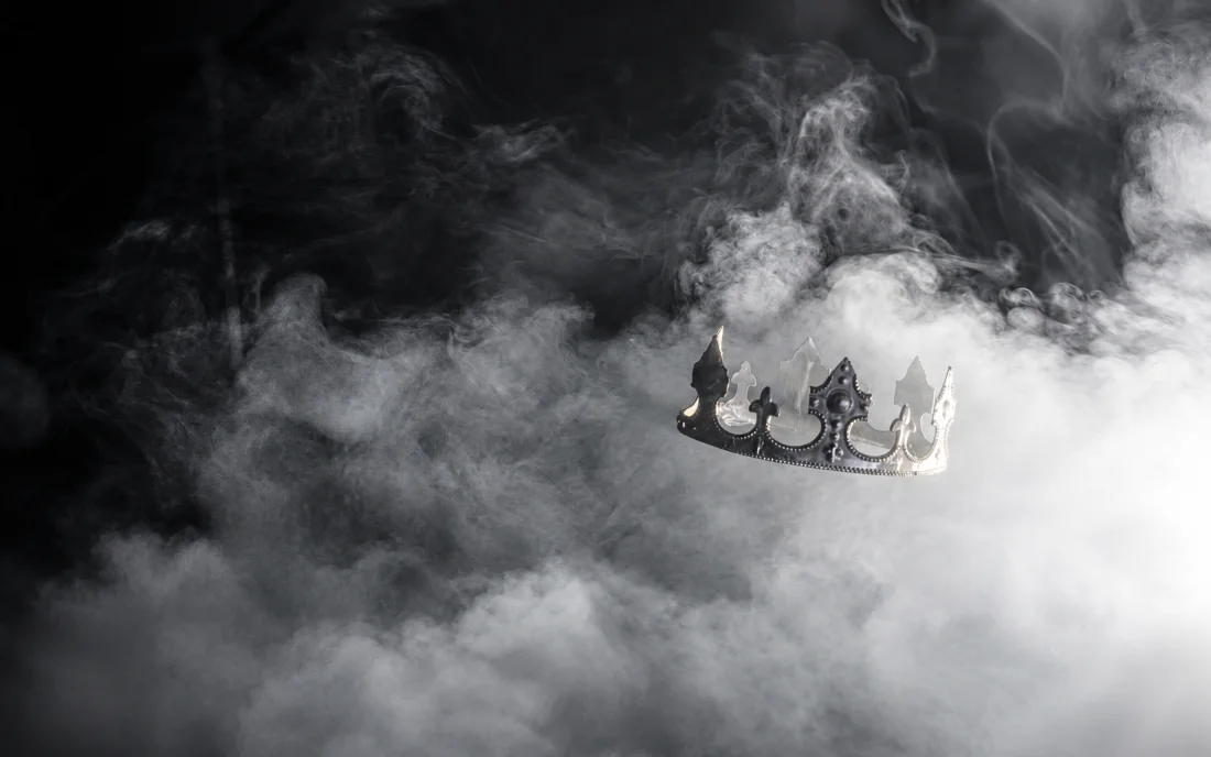 A crown resting in drifting smoke, catching the light from one side.