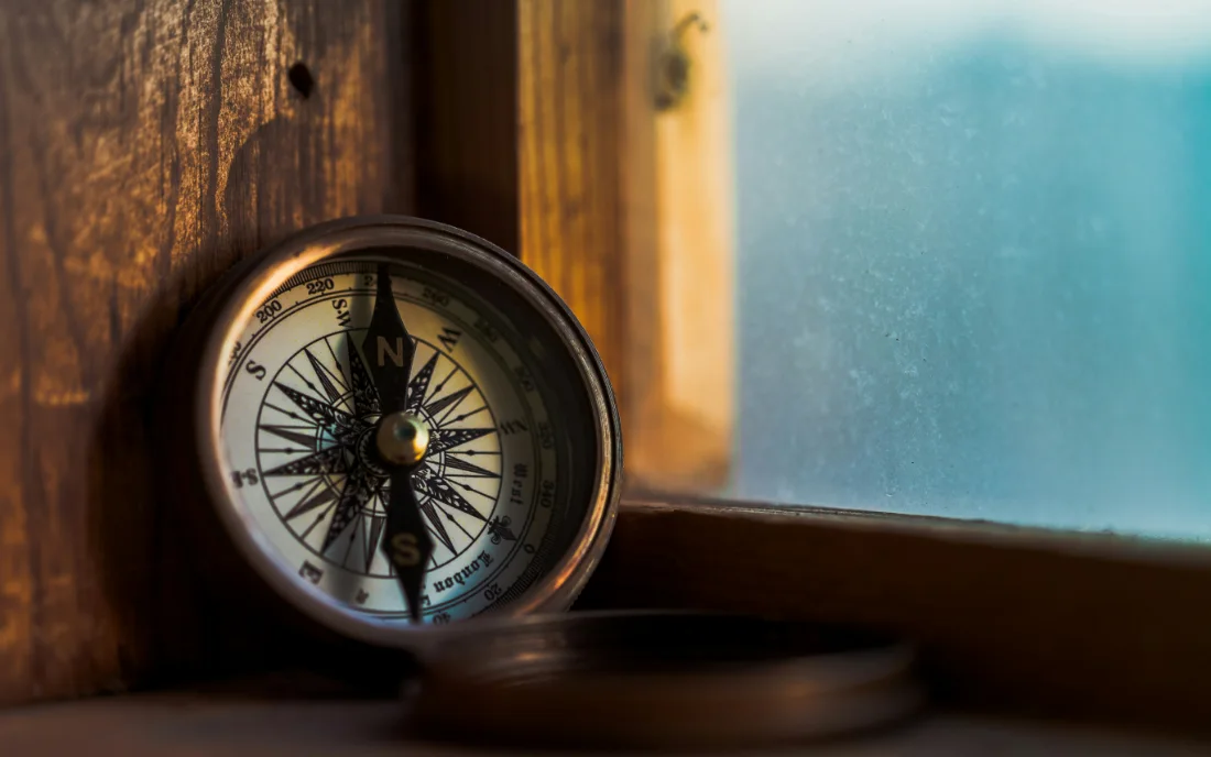A brass compass resting on a windowsill, its needle settled on north.