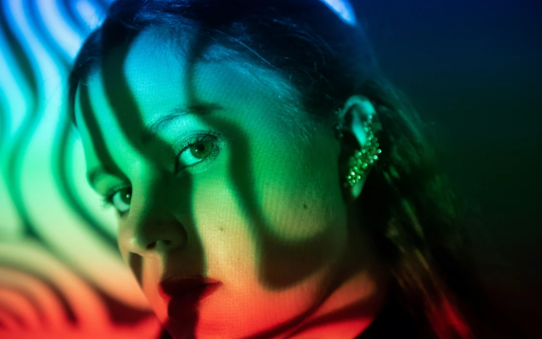 A face lit by bands of projected colour, eyes level with the lens.