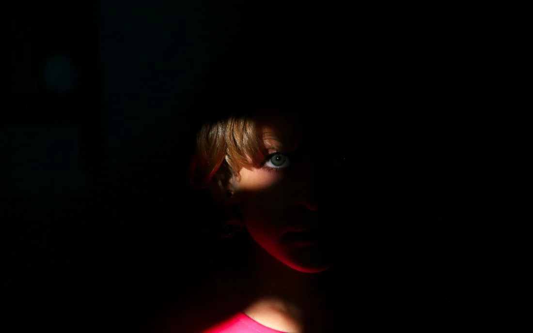 A face in near-darkness, one eye caught by a single light.