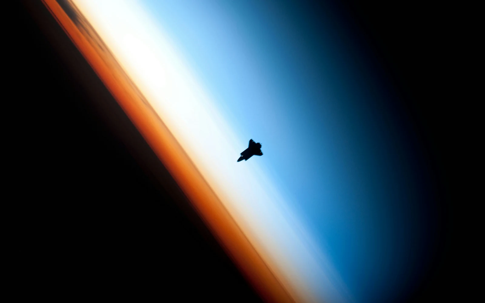 A space shuttle reduced to a silhouette against the light of Earth's atmosphere: remarkable, and easy to miss unless you know where to look.