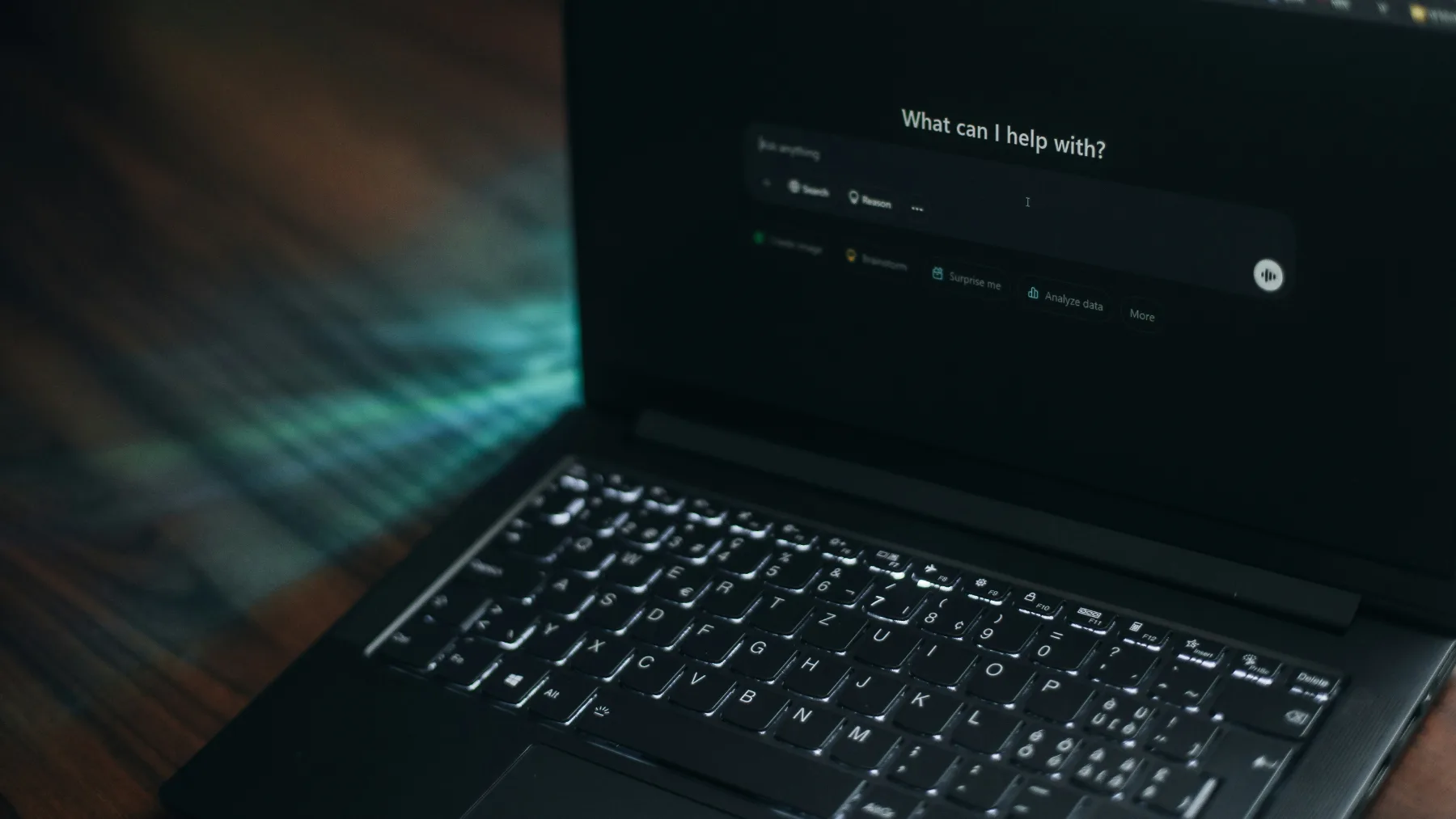 A laptop open on a dark desk, showing an AI assistant waiting for a question.