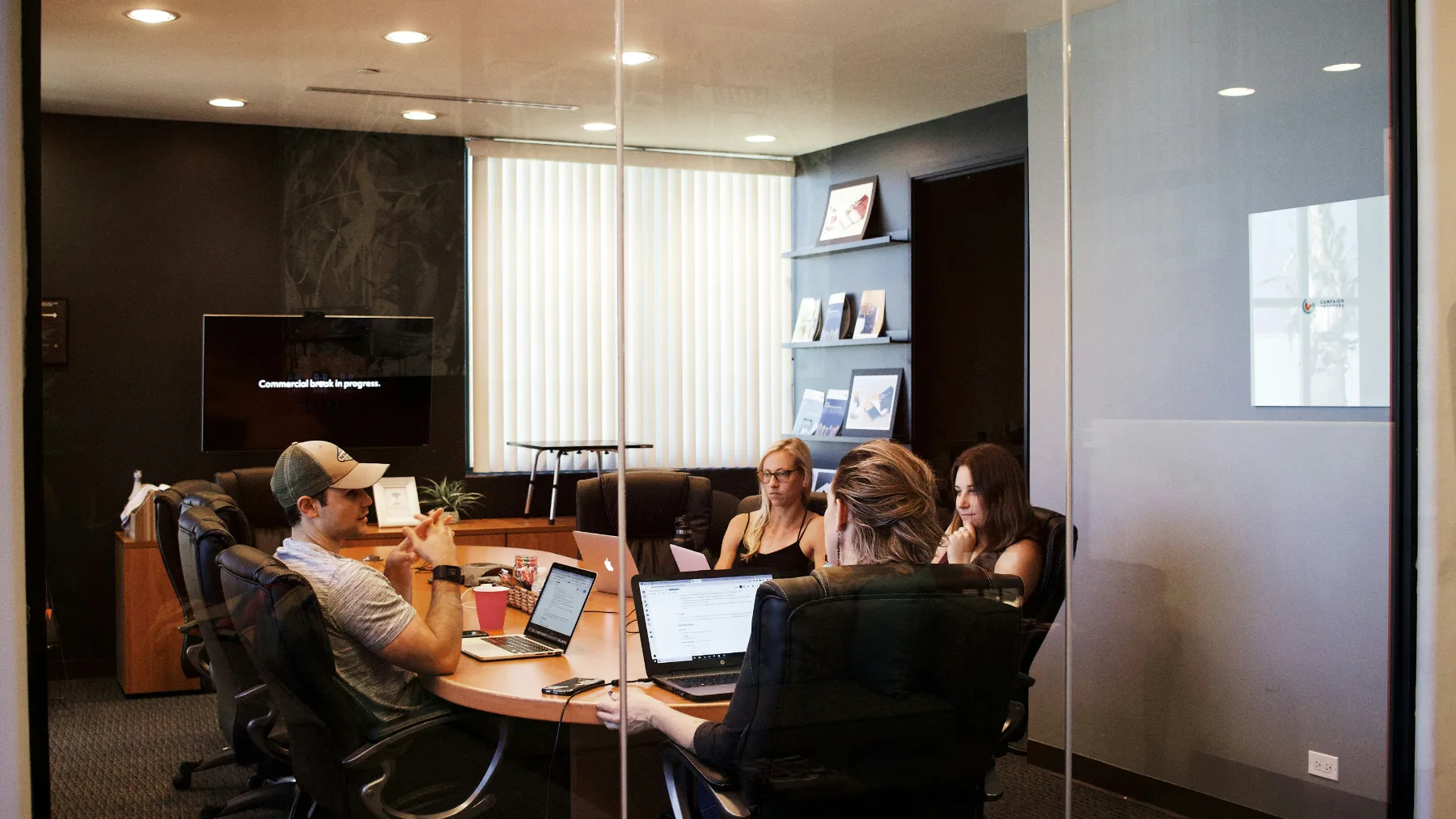 A marketing team working together around a table in a glass-walled meeting room.