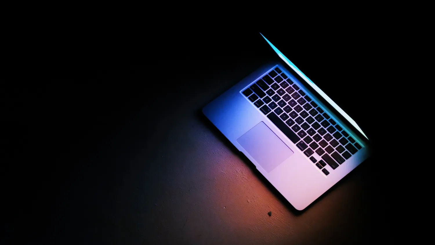 A laptop open in a dark room, lit from the screen.