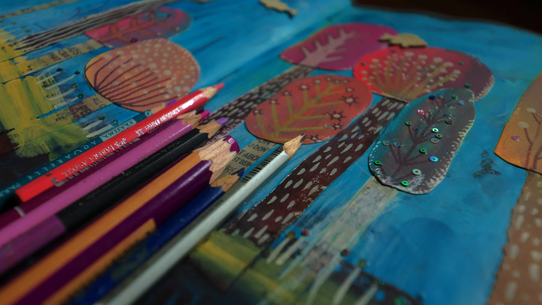 Coloured pencils resting on a hand-painted illustration.