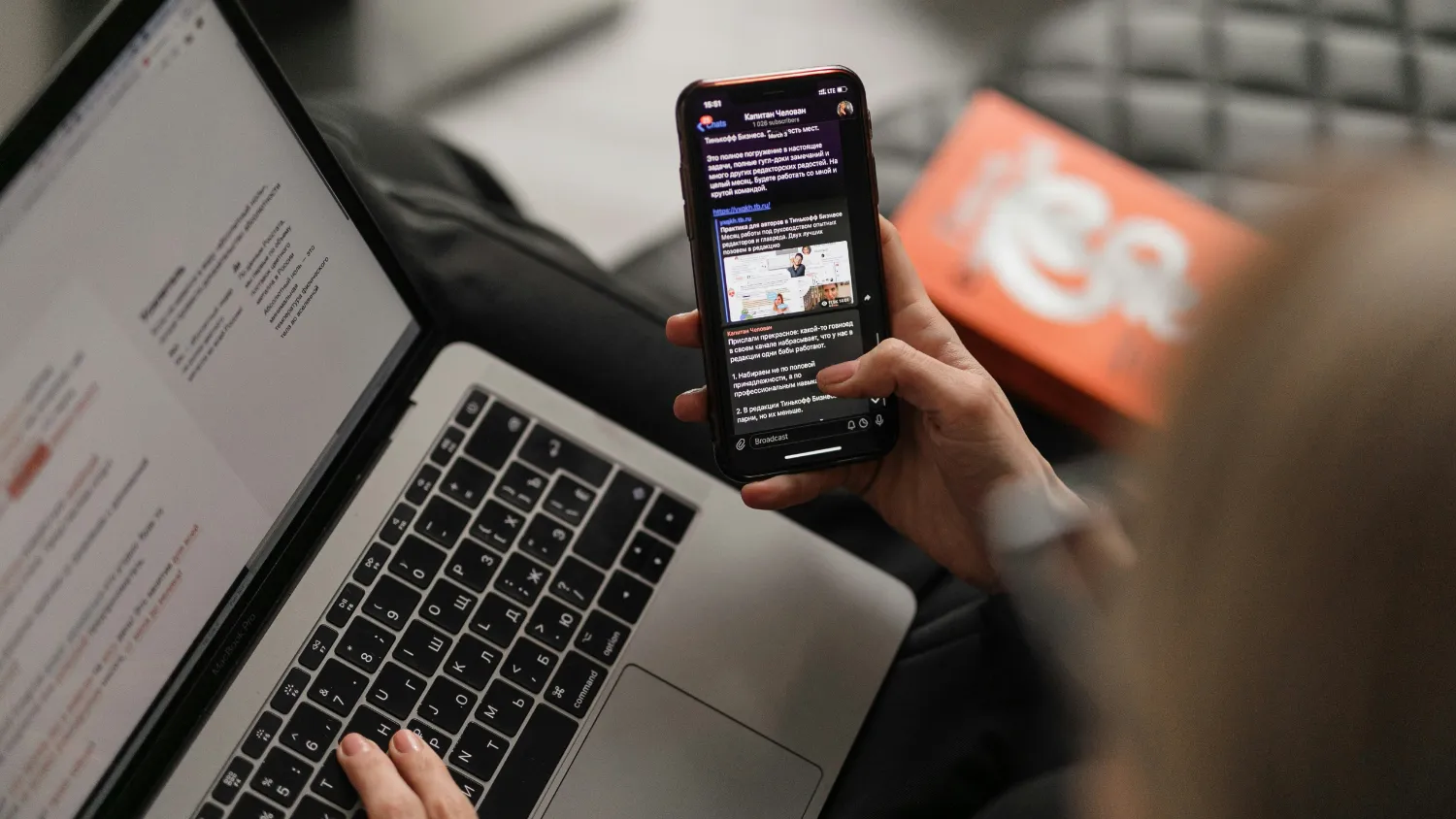 Someone reading a message on a phone beside an open laptop.