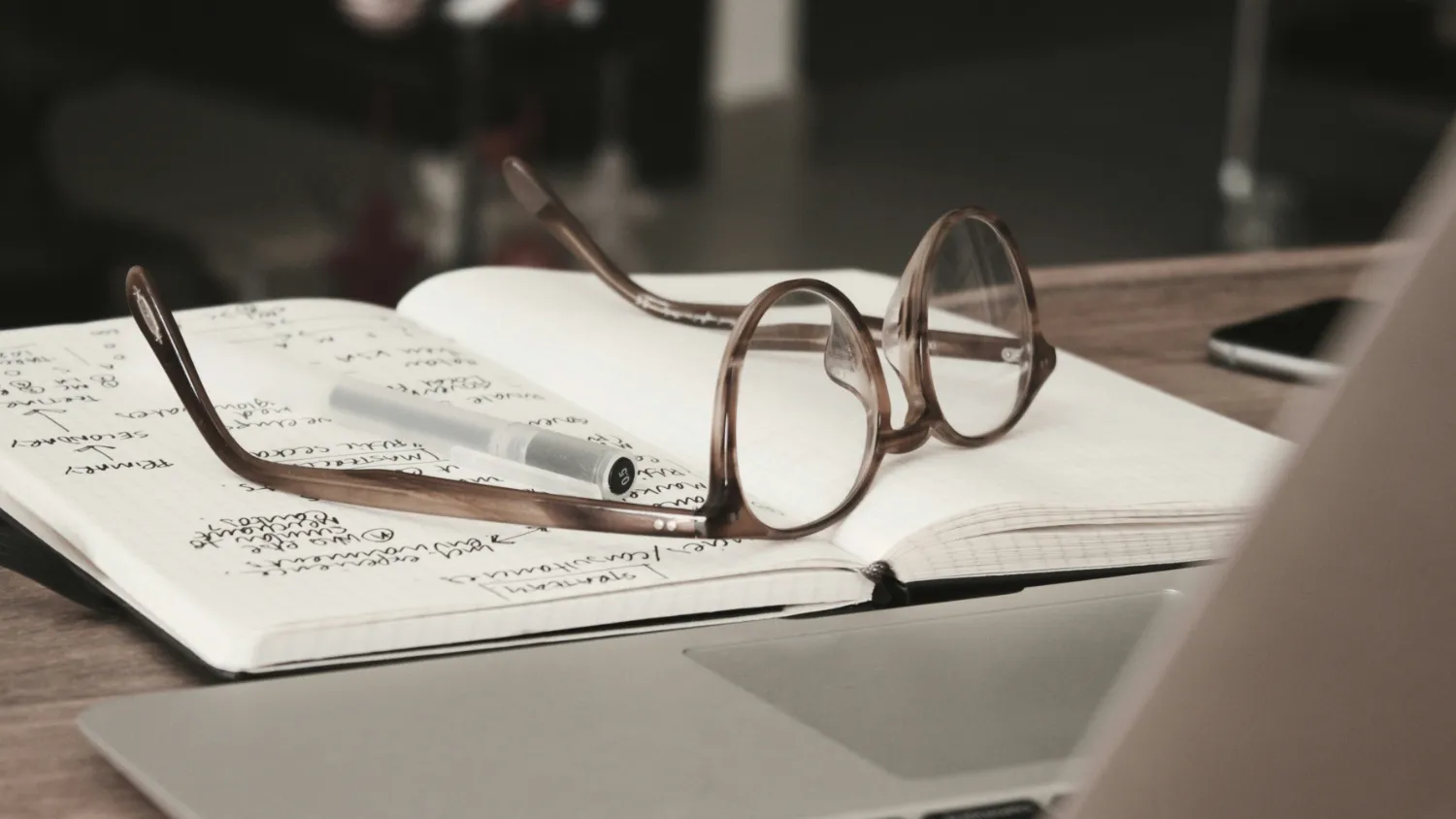 Reading glasses and a pen resting on a notebook of handwritten notes.