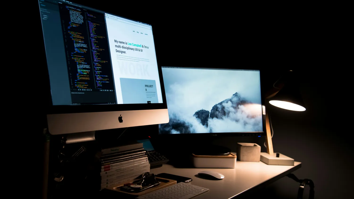 A lit desk at night, code on one screen and a page design on the other.